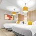 Canario Lagoon Hotel San Juan guest room with two beds, yellow accents, and wicker chair