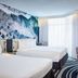 Novotel Toronto North York room with twin beds, ocean wave mural, and desk by bright windows