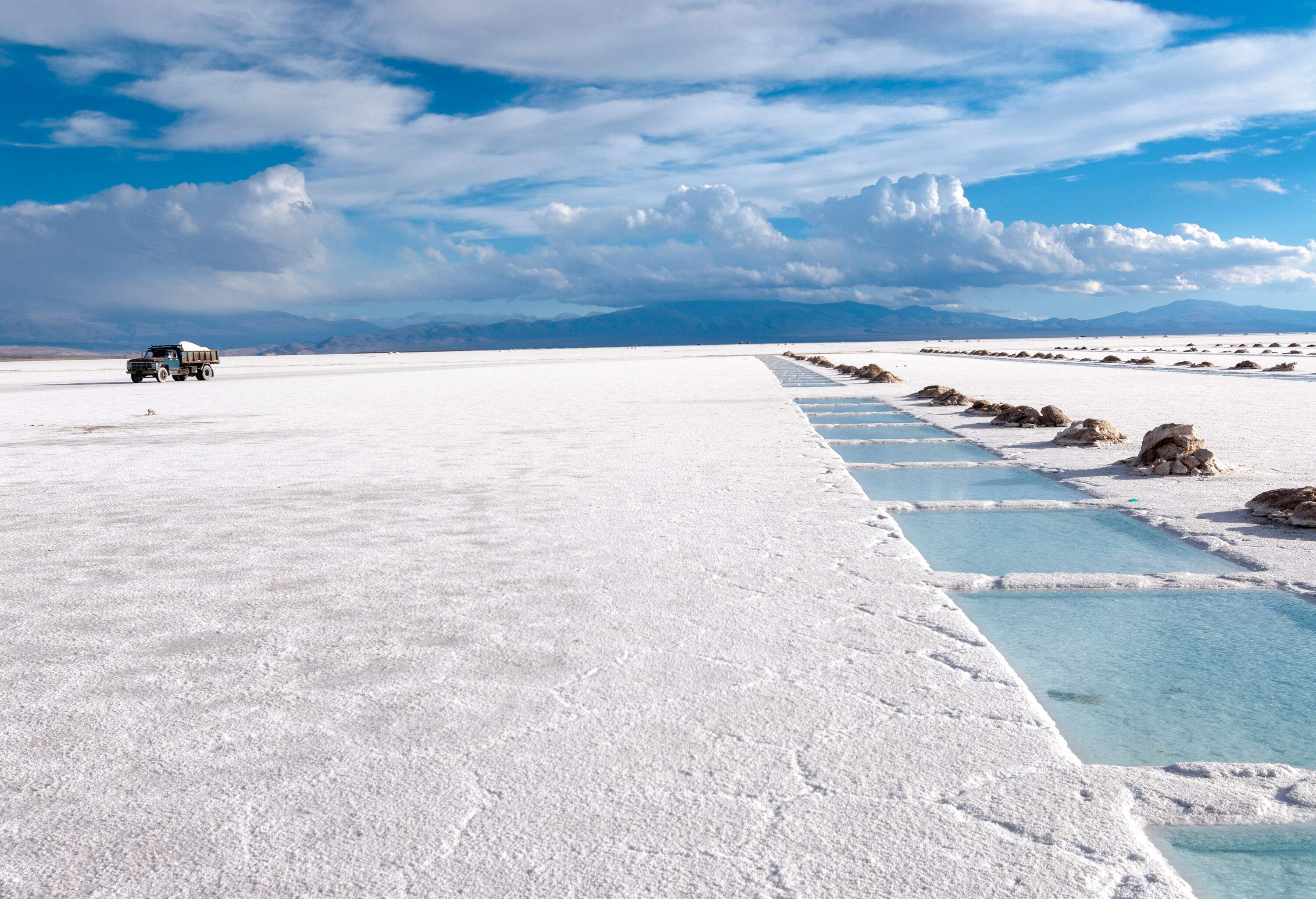 Salt extraction pools create a unique white landscape, with a truck filled with salt travelling in the background.