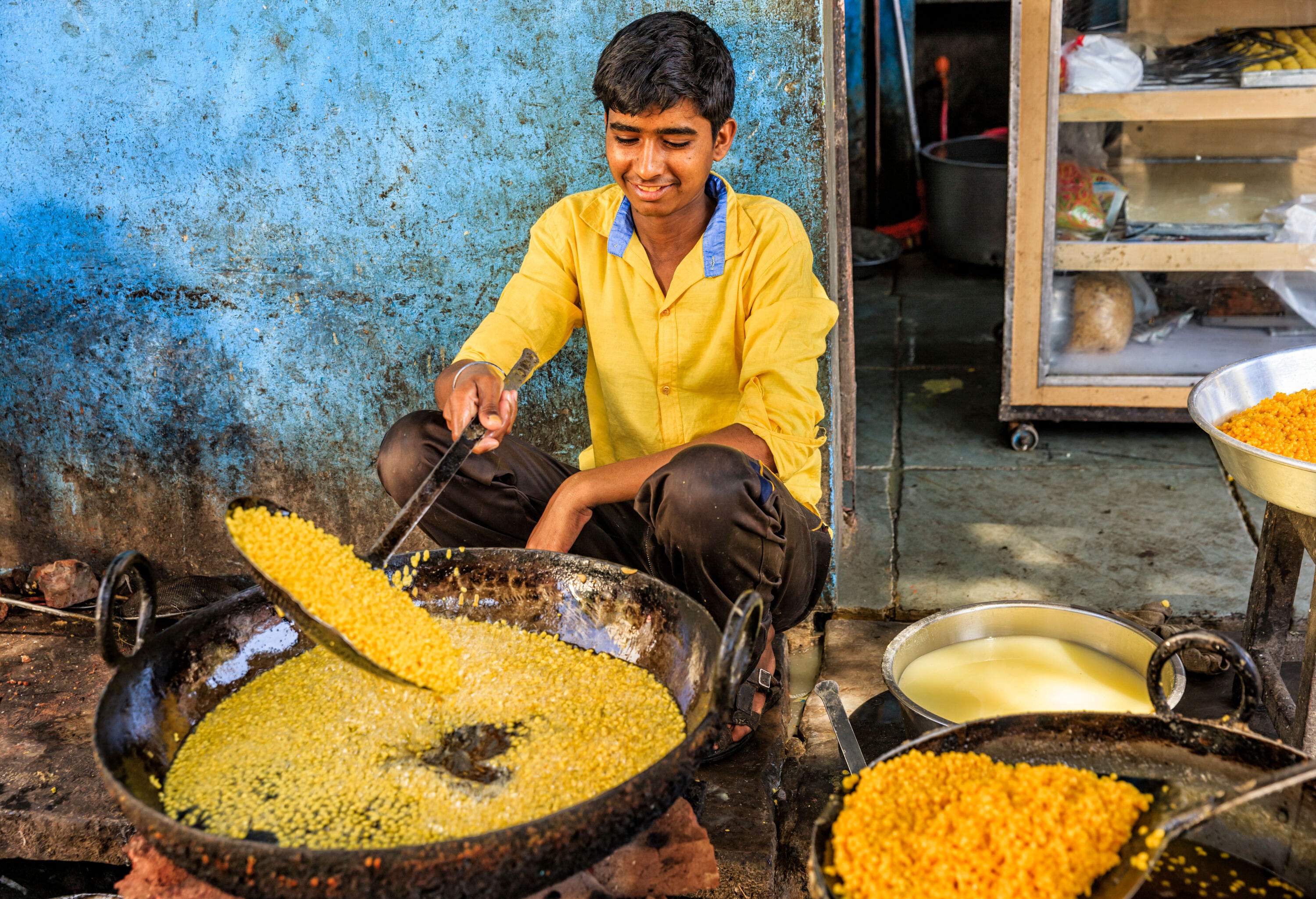 A young Indian boy donning vibrant yellow clothes diligently prepares delectable street food.