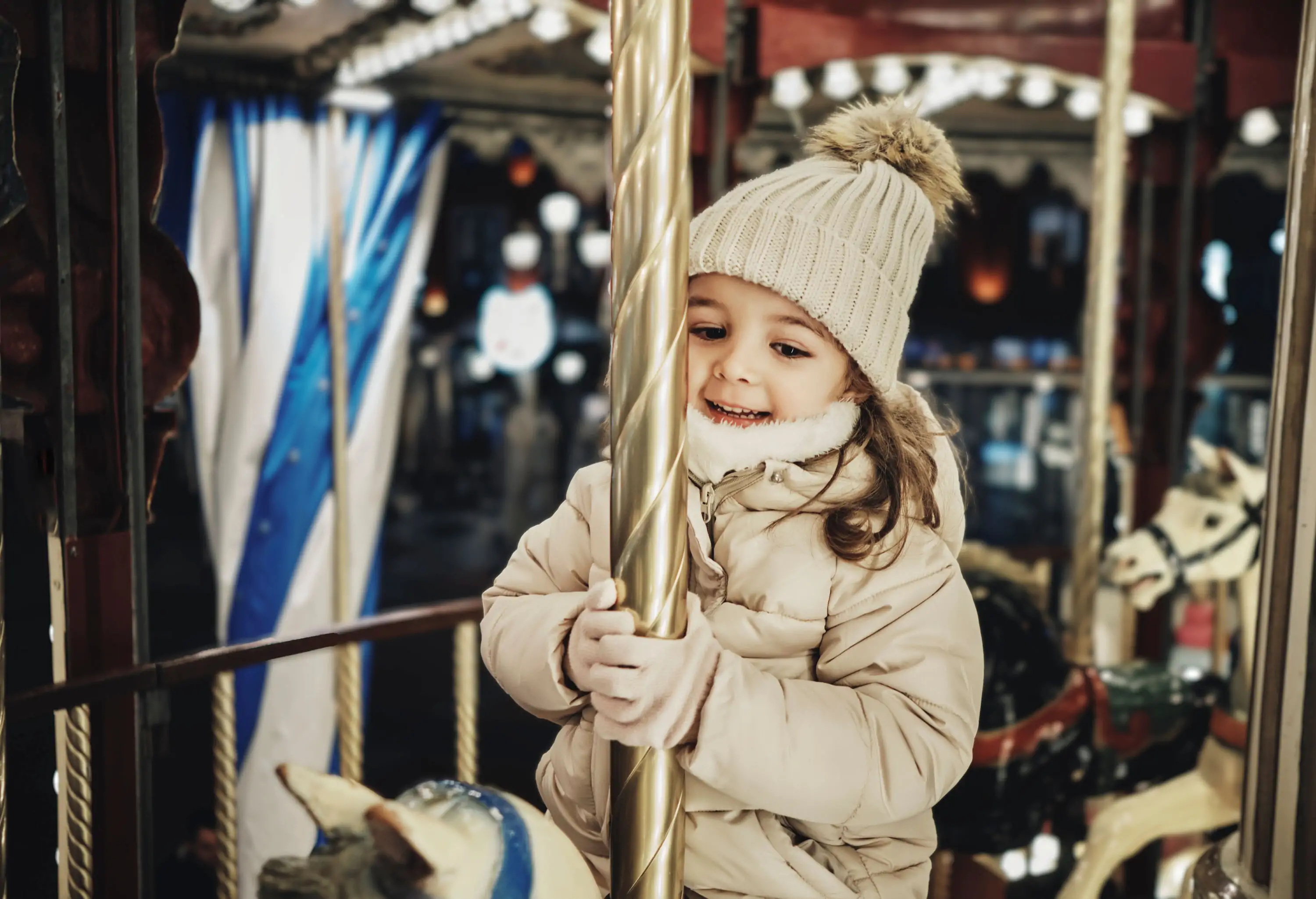 A happy little girl rides on a horse in a carousel.