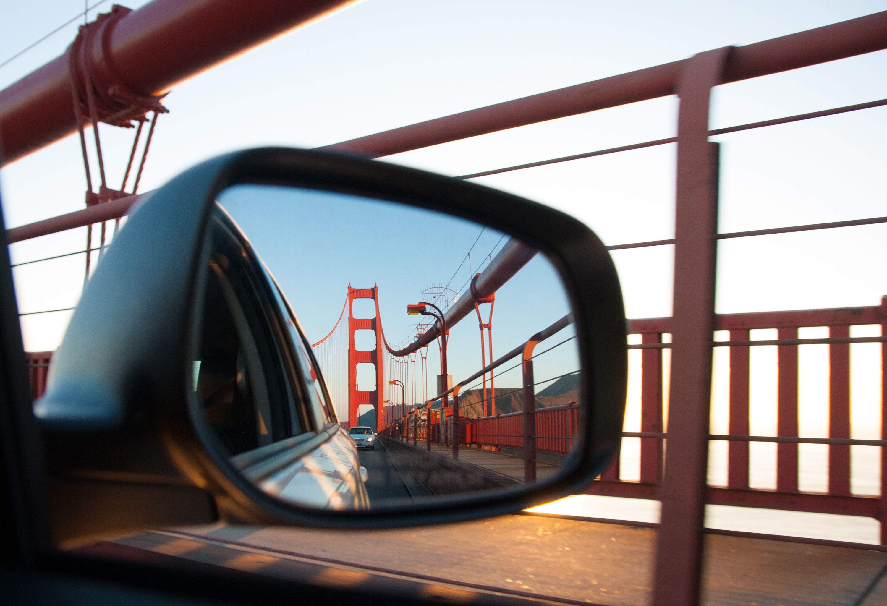 The iconic Golden Gate Bridge is captured in the reflection of a car's side mirror.