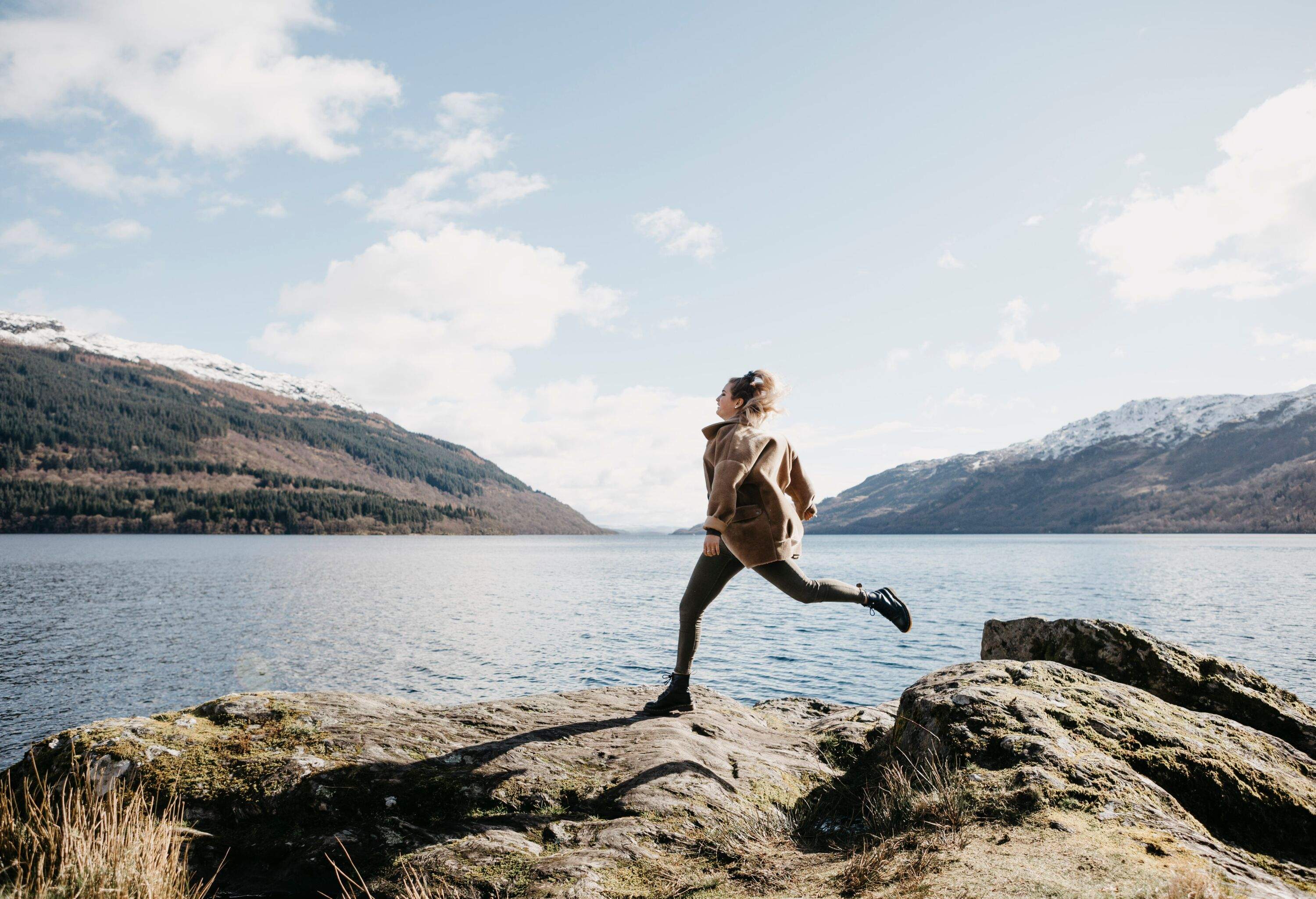 Woman running amongst rocks overlooking Loch Lomond in Scotland