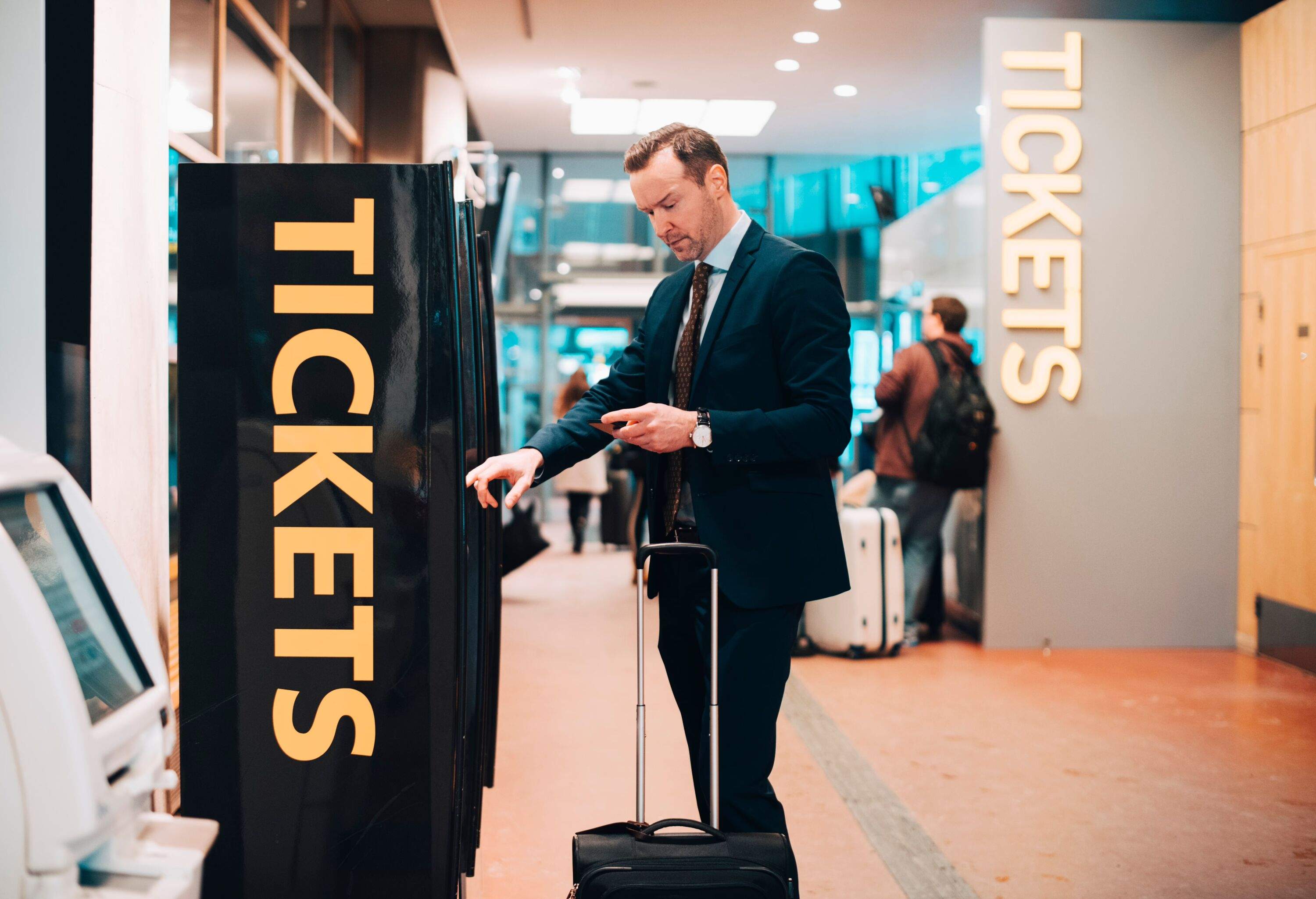 Businessman with suitcase at airport buying train tickets