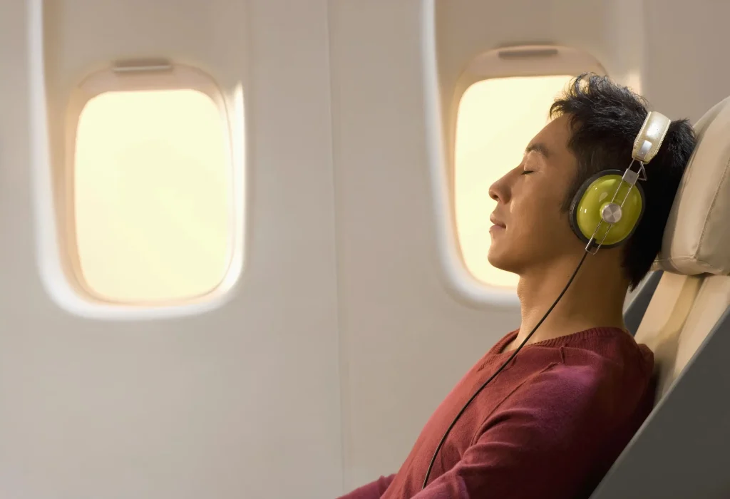 A man on an airplane, listening to music with his eyes closed.